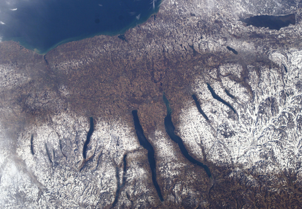 Long, narrow lakes lie amid snow-covered terrain in a view from space.
