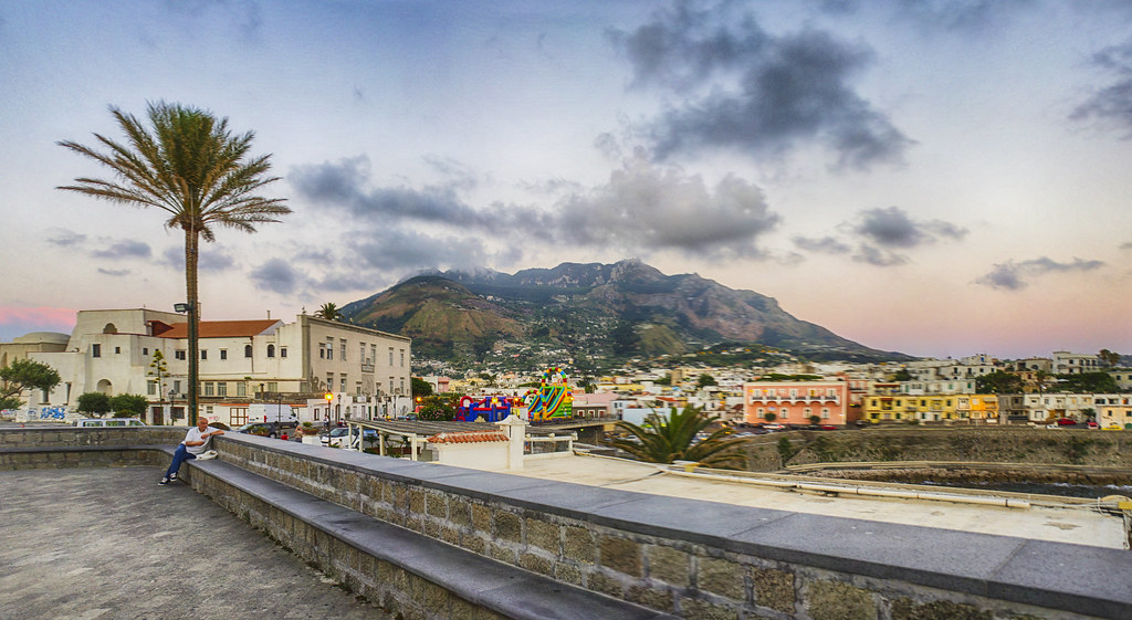 Mount Epomeo rises behind buildings and a waterfront on Ischia.