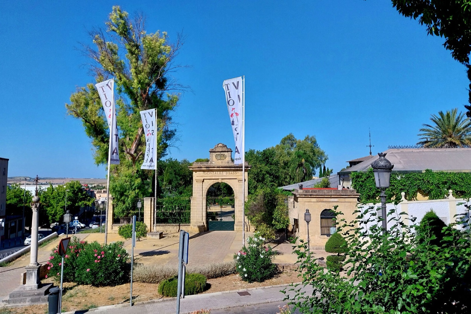A bodega complex with tiled roofs, gardens, and a stone entrance stands beneath a clear blue sky.
